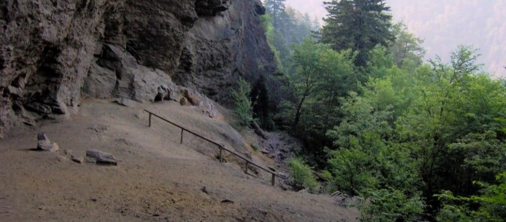 A wide, barren ledge hugs the base of towering rock walls above the forested slopes of Great Smoky Mountains National Park.