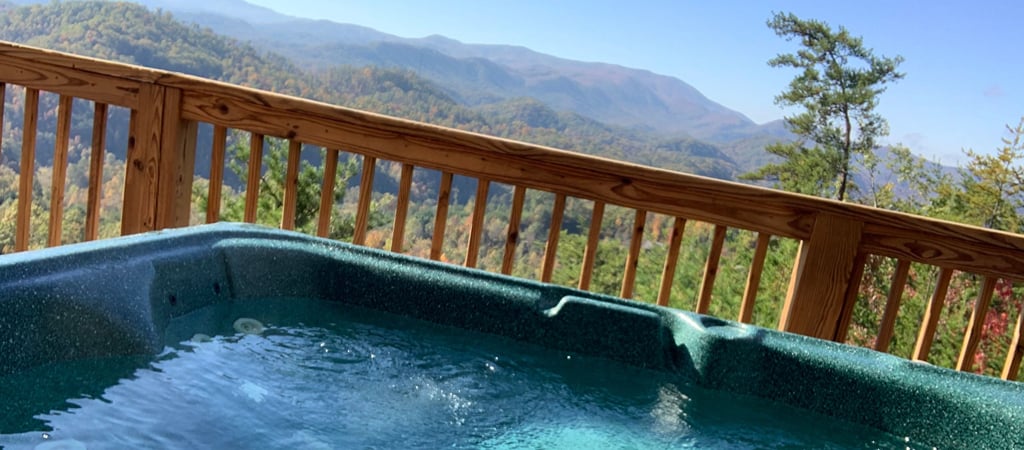 A hot tub sits on a cabin deck overlooking colorful fall Smoky Mountain views.