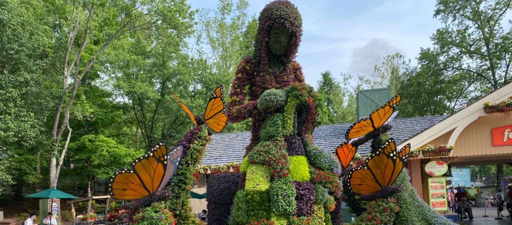 Plant sculpture of a woman quilting, surrounded by large butterfly