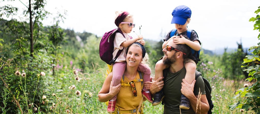 Family Wildflower Hike A mother with a young daughter on her shoulders and a father with a young son on his shoulders hike through wildflowers.