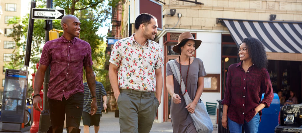 A group of young adults smile at each other while walking downtown on a nice day.