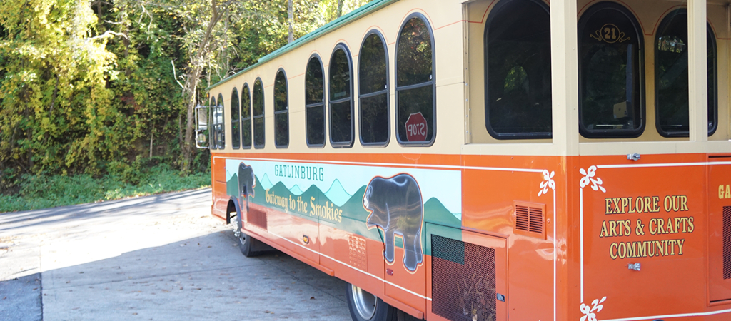 A parked Gatlinburg Trolley bus on a sunny day reads Explore Our Arts & Crafts Community.