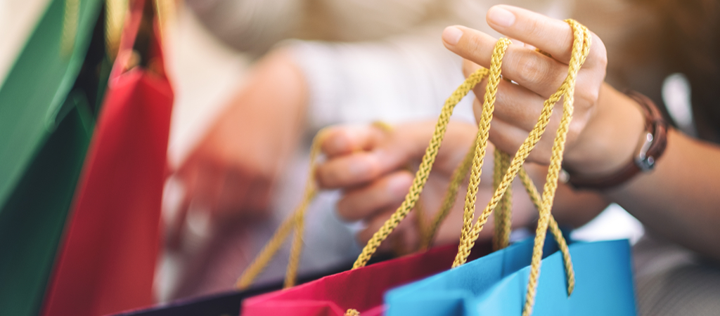 Hands Holding Shopping Bags A close-up of a woman's hands holding colorful shopping bags, with another person holding more shopping bags in the background.