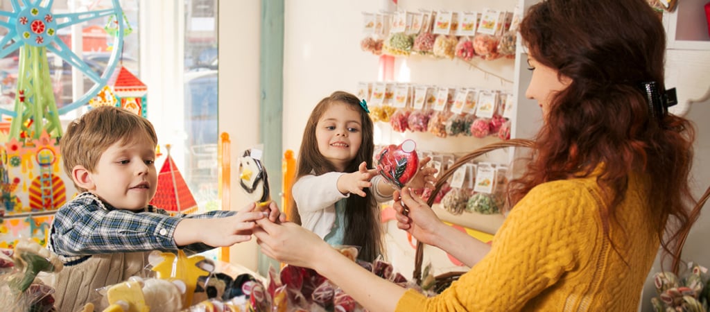 Happy Kids Receiving Candy from a Shopkeeper Two children eagerly reach for candy from a female shopkeeper at a local candy store.