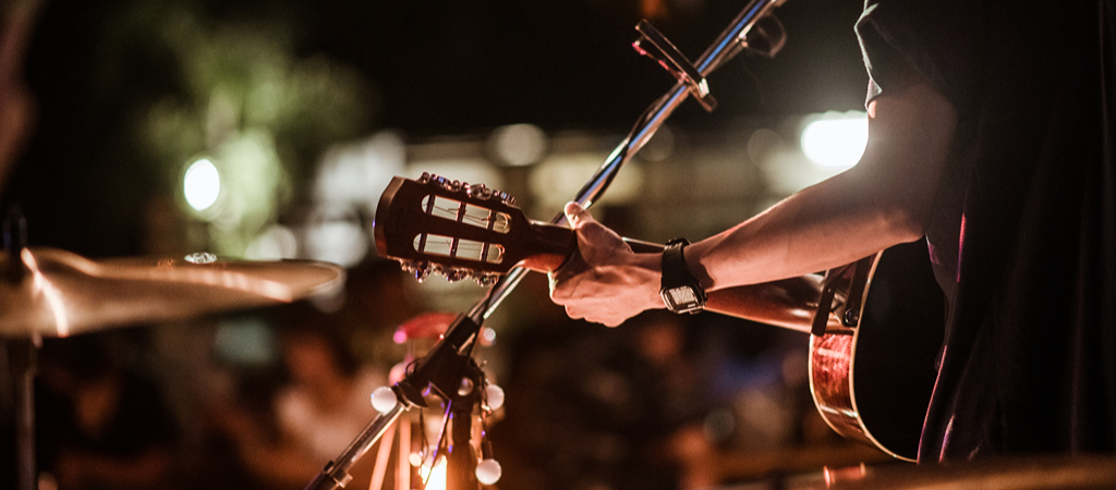 A close-up of a man's arm playing guitar on stage at night.