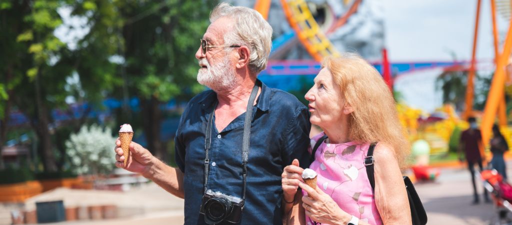 Older couple eating ice cream and looking around at an amusement park.