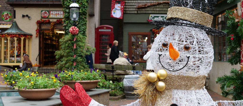 A snowman Christmas decoration smiles and welcomes visitors to The Village Shops in Gatlinburg, with more holiday decor around the shops in the background.
