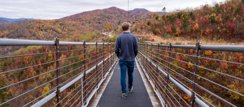 Young Man Crossing Gatlinburg SkyBridge in Fall A young man walks the Gatlinburg SkyBridge, with stunning colorful leaves adorning the valley and Smoky Mountain peaks in fall.